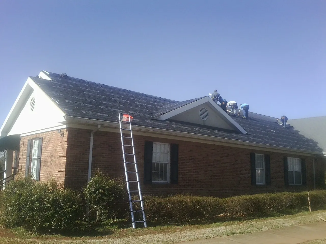 Crew tearing shingles off a brick ranch roof with a ladder set — Metal Roof Repair work by our crew in Stratford