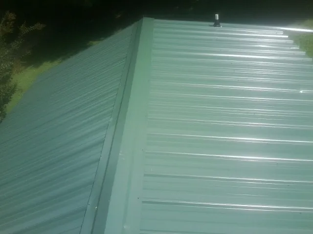 New green metal panels meeting at the ridge of a roof — Flat Roof Repair work by our crew in Stratford