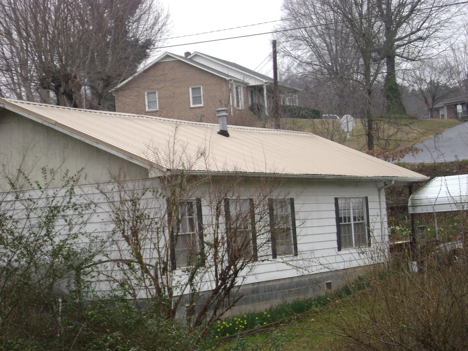 Tan metal roof on a white sided house set into a hillside in Stratford